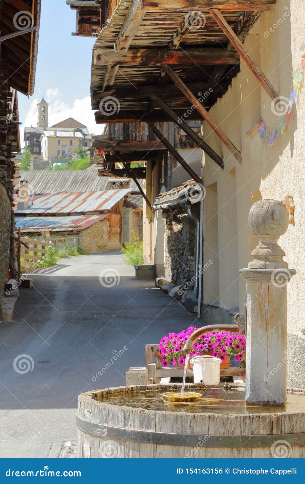 a traditional wooden fountain with traditional wooden balconies and the church in the background in saint veran village