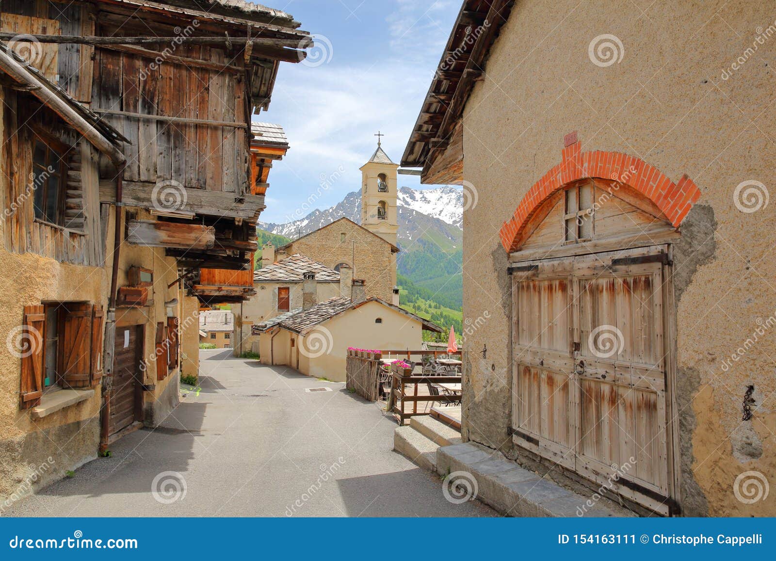 traditional wooden houses and the church in saint veran village, with mountain range covered with snow in the background