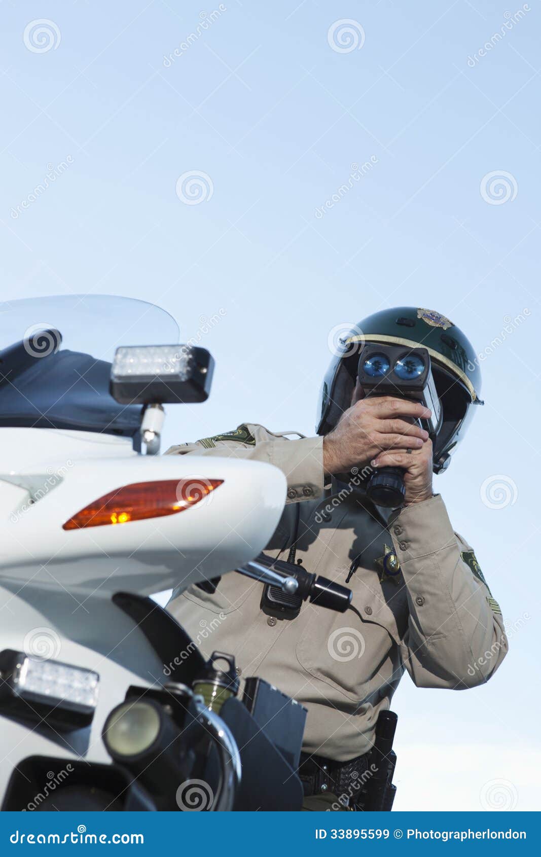 Low angle view of middle aged traffic cop monitoring speed through radar against sky