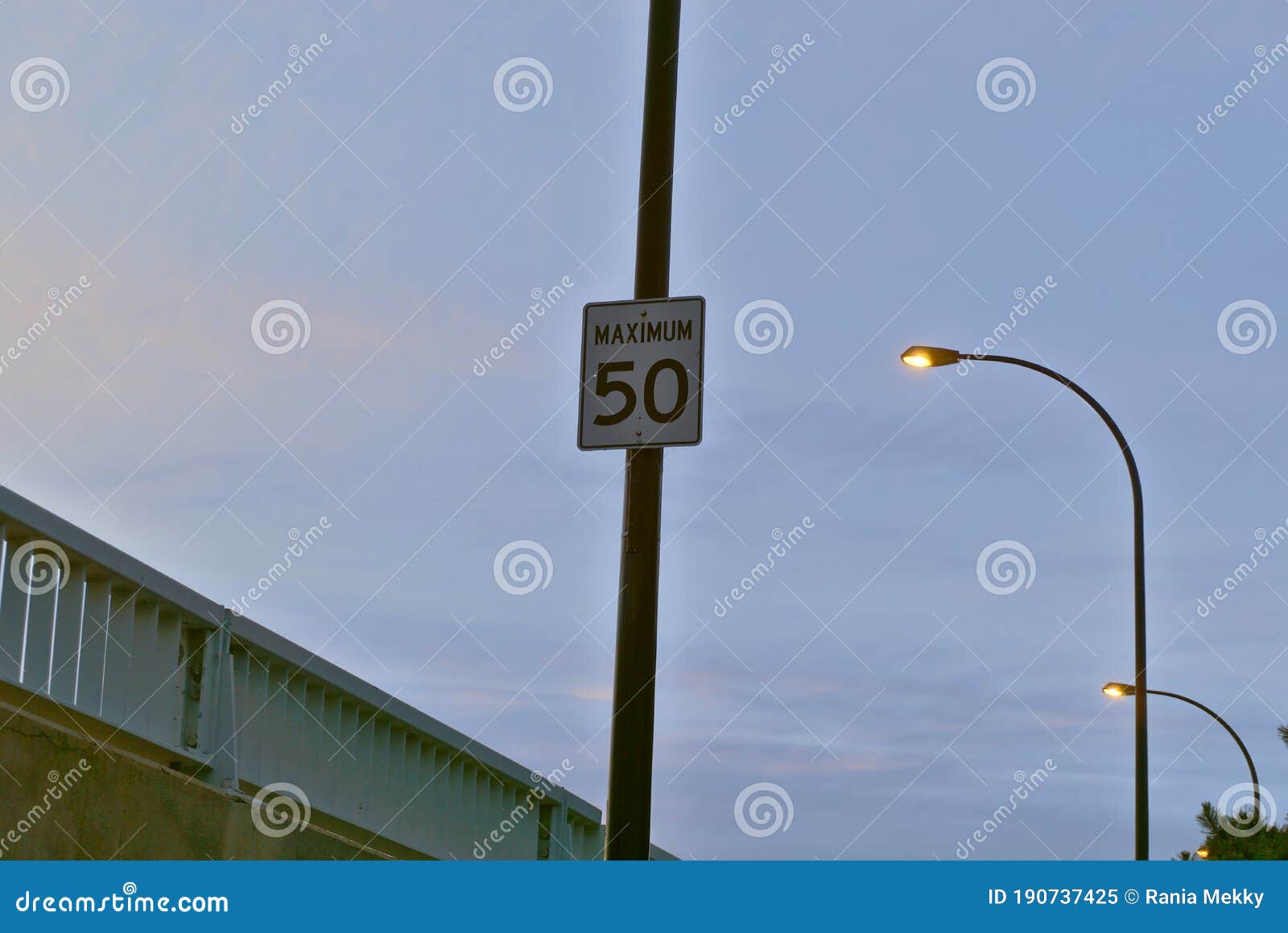 a traffic sign speed limit of 50 km/hr in a sector over a bridge with a background of a cloudy blue sky and street light