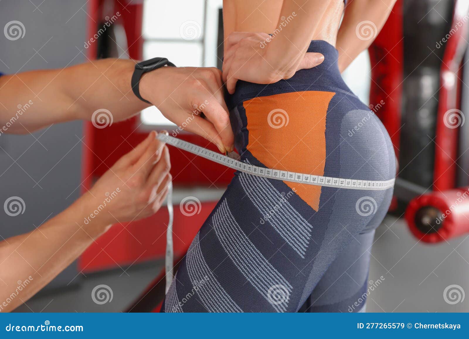 trainer measuring woman`s hips with tape in gym, closeup