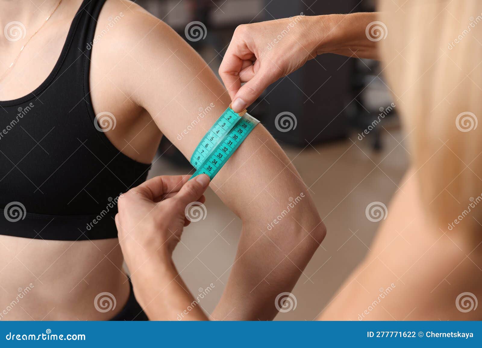 trainer measuring woman`s triceps with tape in gym, closeup