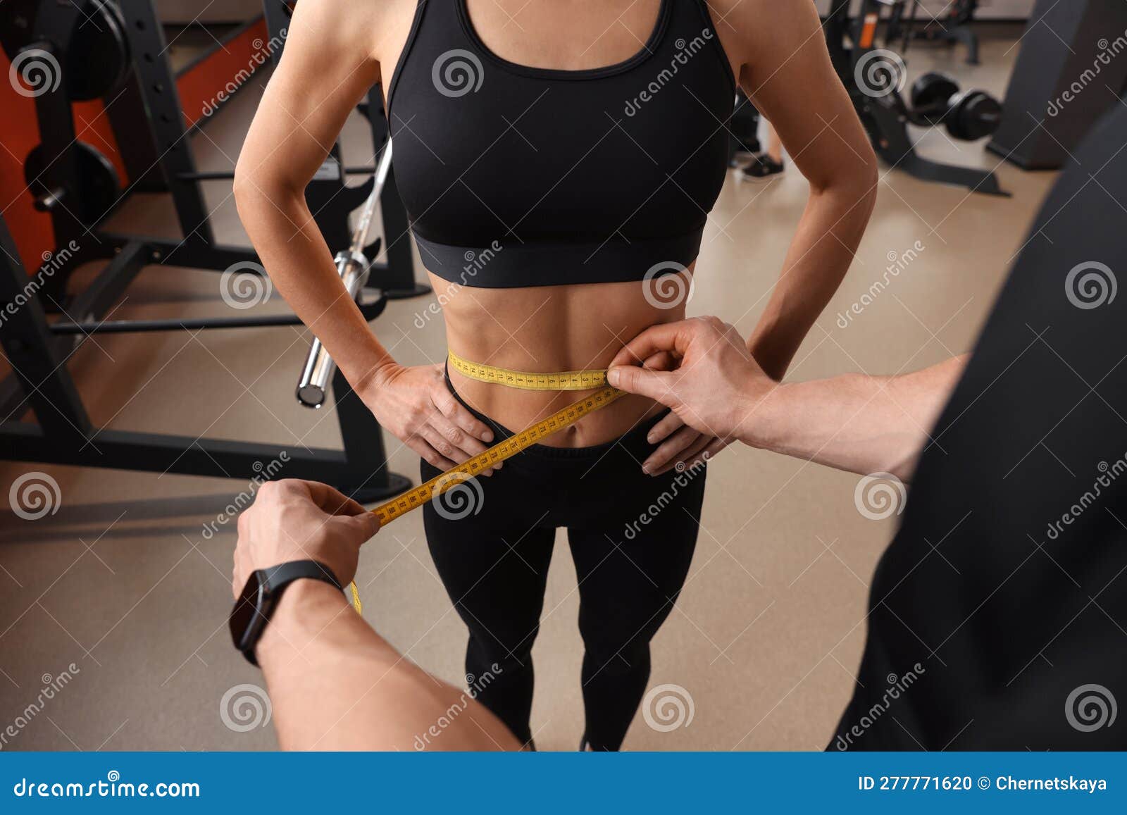 trainer measuring woman`s waist with tape in gym, closeup