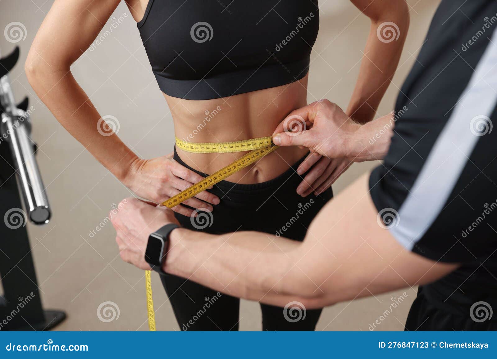 trainer measuring woman`s waist with tape in gym, closeup