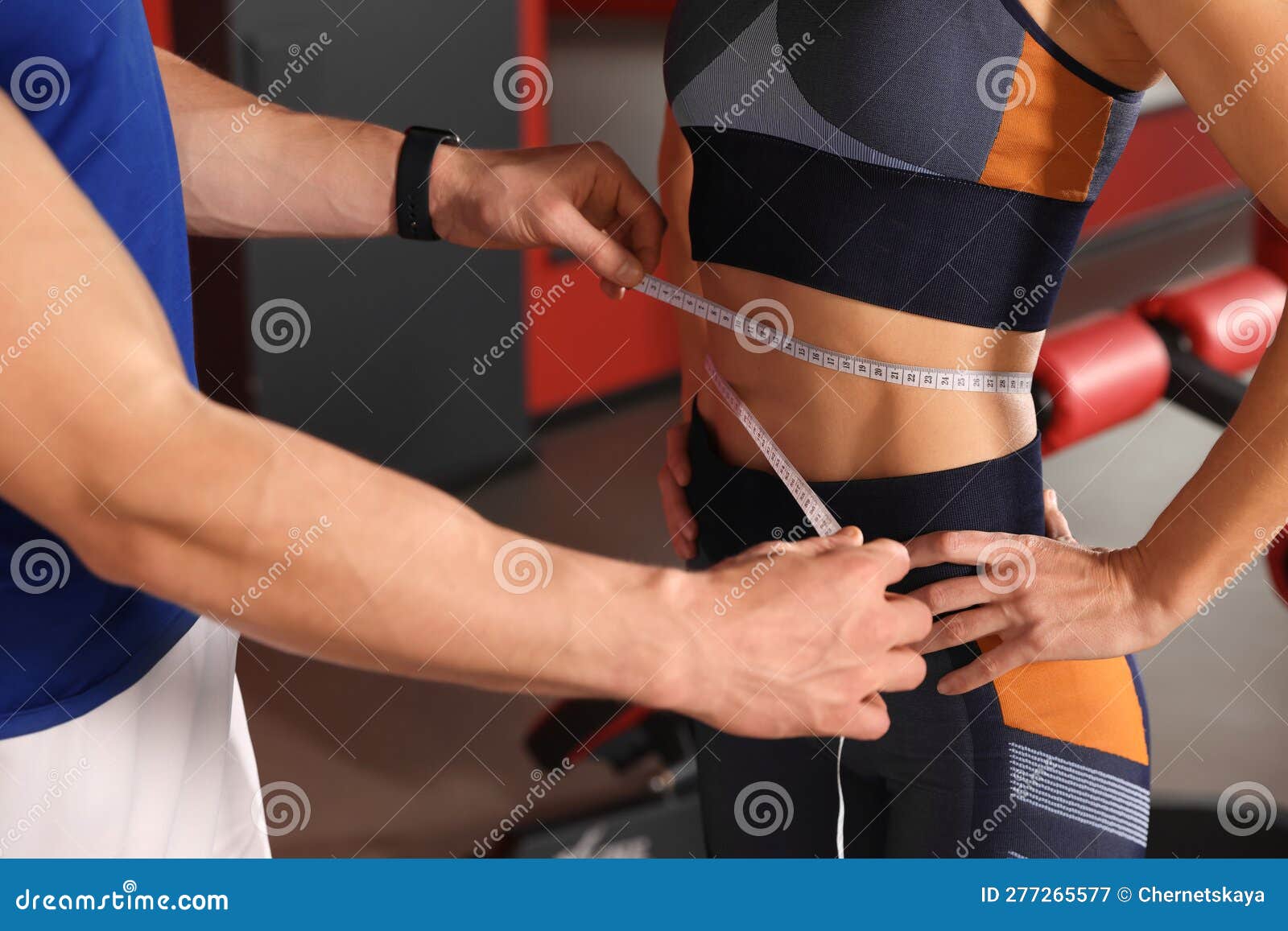 trainer measuring woman`s waist with tape in gym, closeup