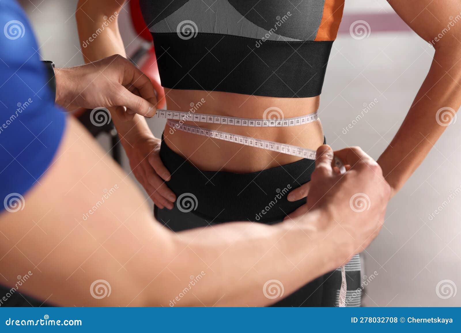 trainer measuring woman`s waist with tape in gym, closeup