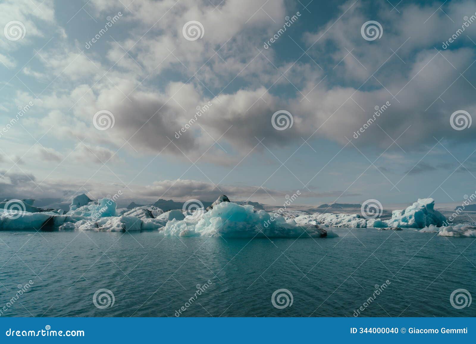 wide-angle view of floating icebergs on a glacial lake with distant mountains under a soft sky