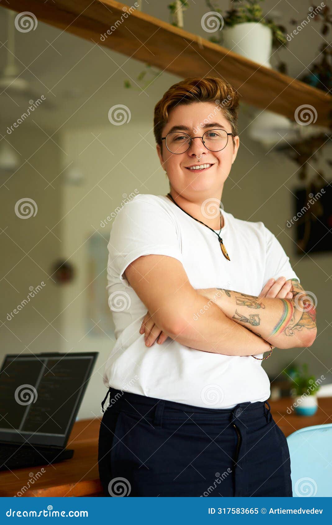 confident transgender pro in office attire stands with arms folded, smiling at camera. trans exec in well-lit workspace