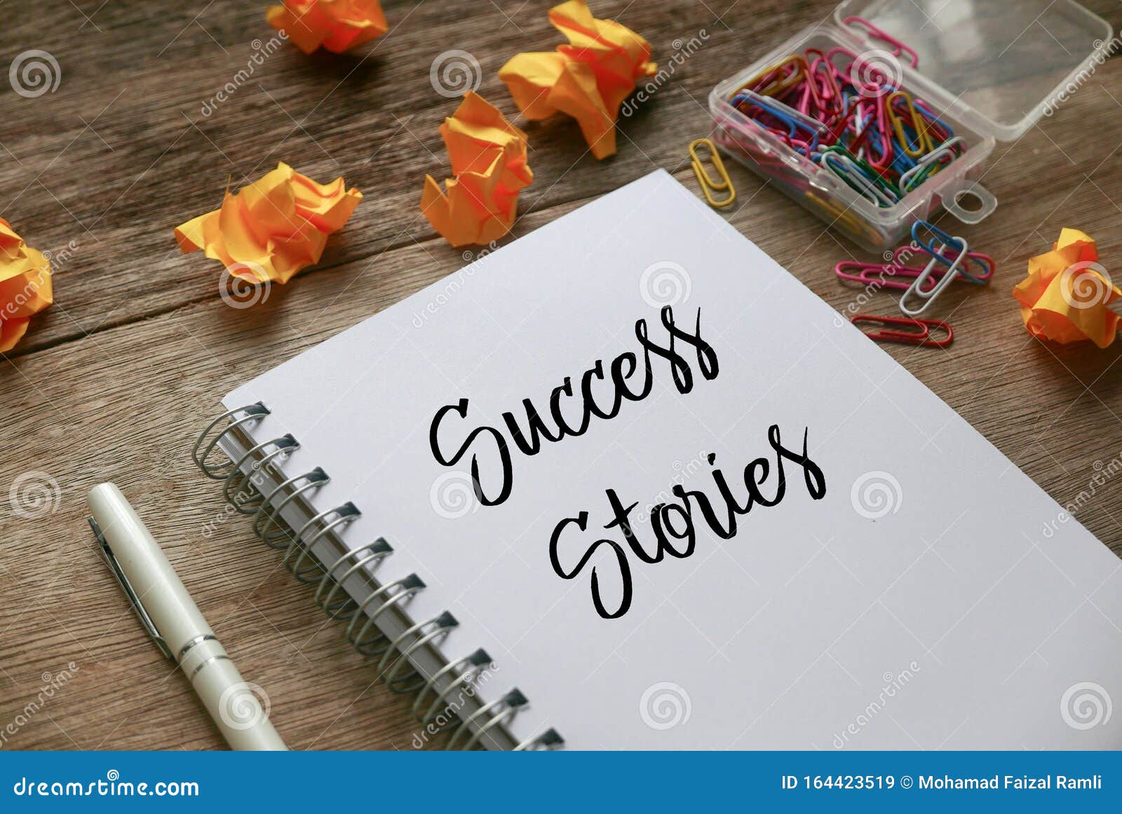 trash paper, paper clips,pen and notebook written with success stories on notebook on wooden background