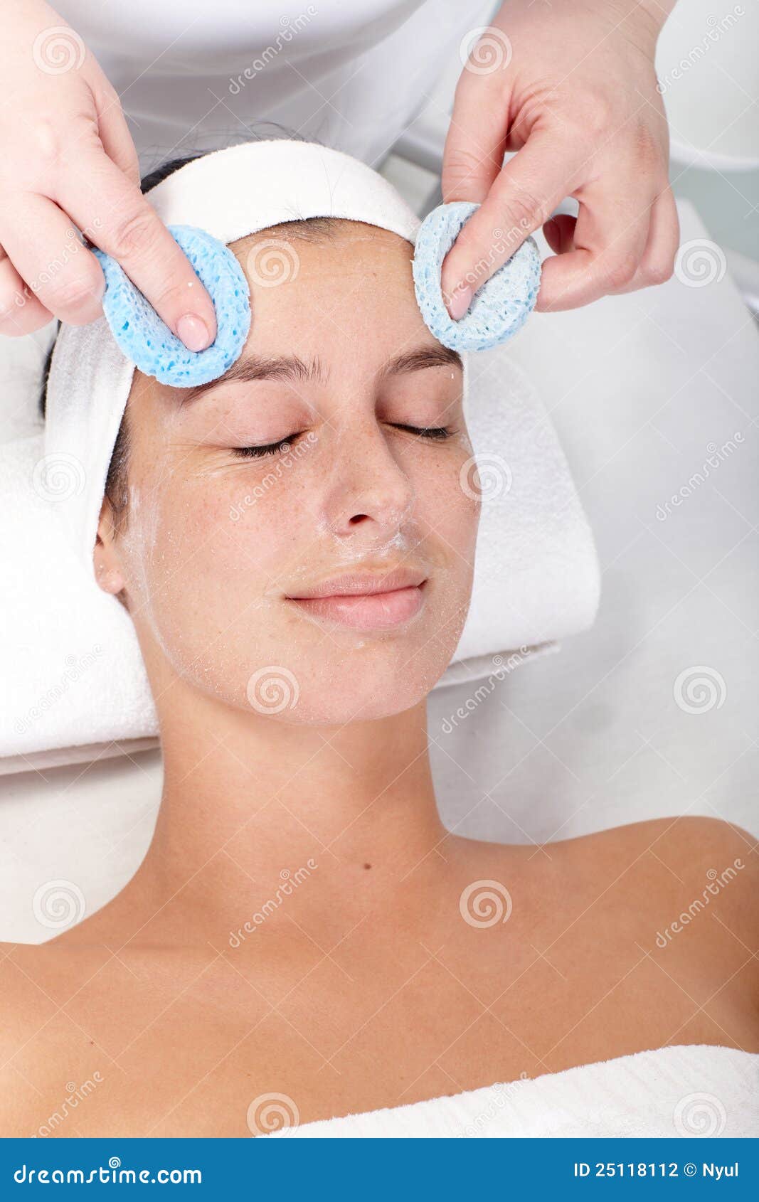 Tratamiento facial de la belleza. Beautician que quita la crema facial por la esponja de la cara de la hembra.