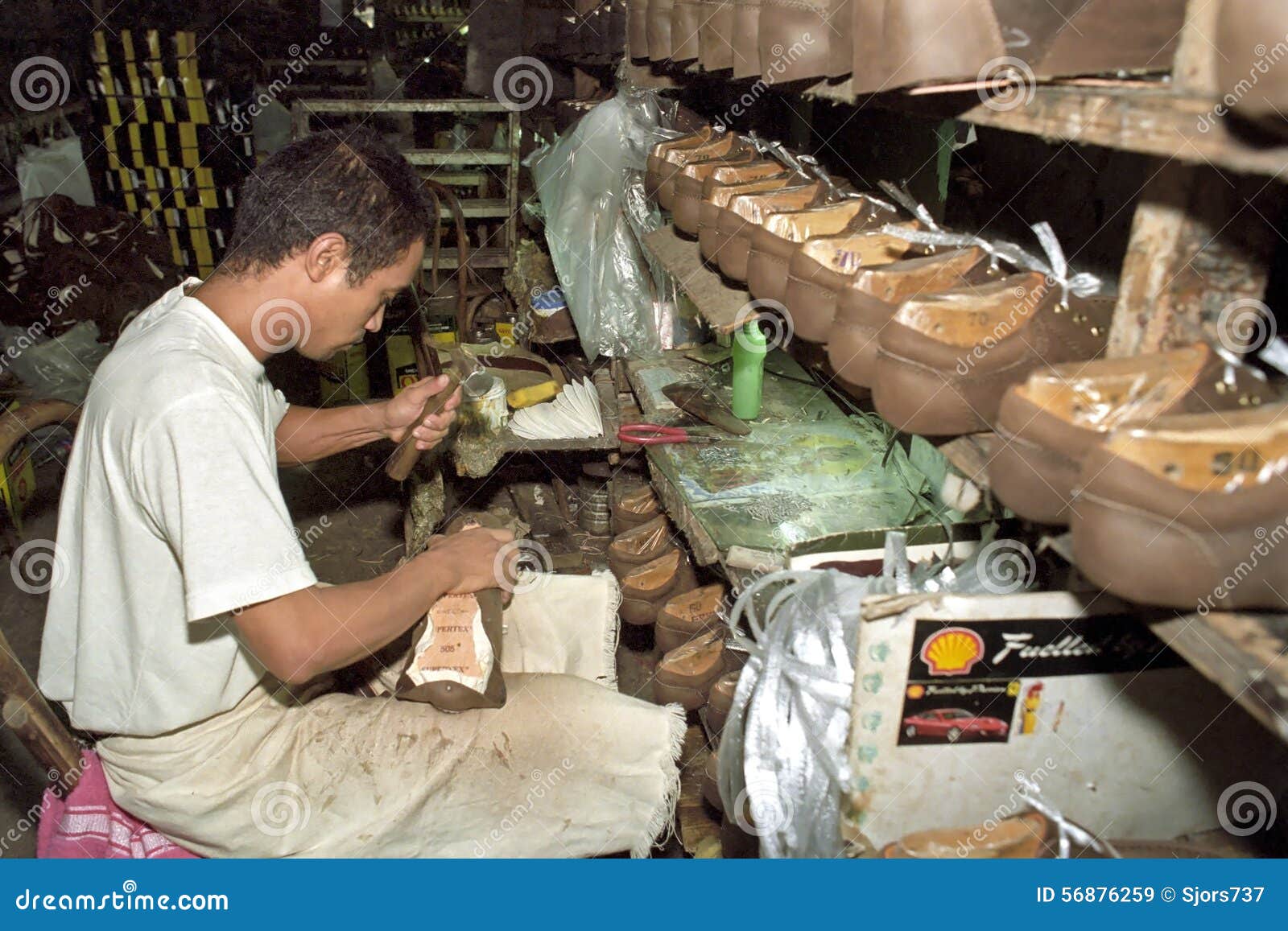 Travailleur philippin travaillant dans l'usine de chaussure. Philippines, île Luçon, région de capital national de métro Manille, ville de Marikina : un homme travaille dans l'usine de chaussure La fabrication des chaussures, chaussures, est en grande partie travail manuel Peu d'outil est utilisé et l'espace de travail, lieu de travail est tout à fait foncé Ce travailleur de salaire martèle avec un marteau