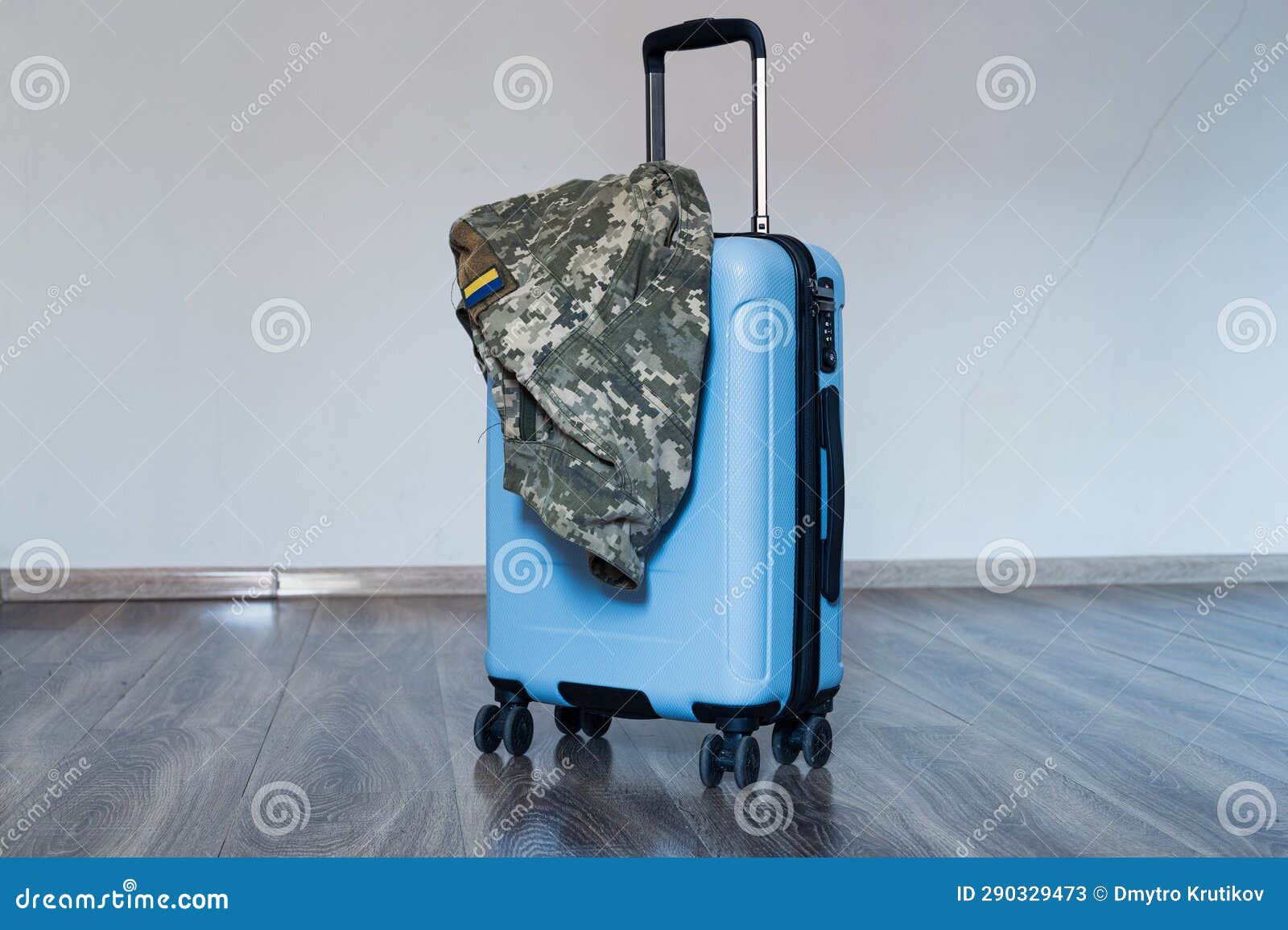 travel blue suitecase stands on wooden floor with ukrainian military pixel uniform jacket