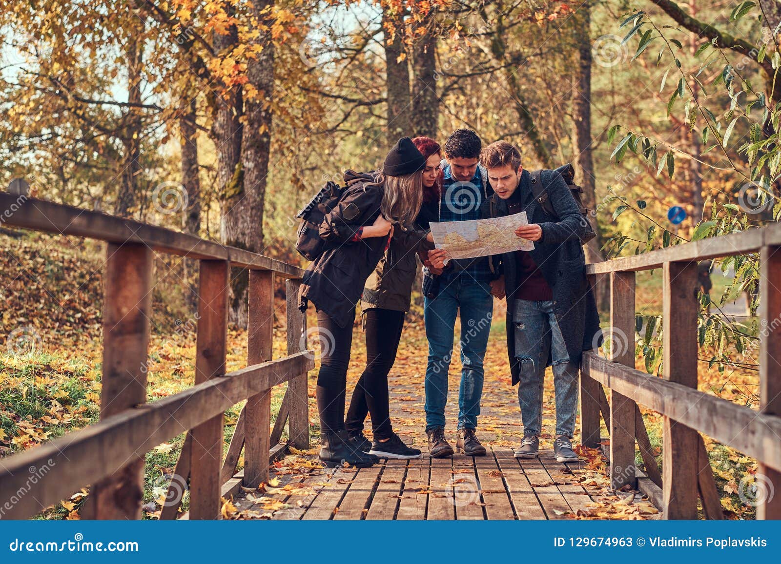 group of young friends hiking in autumn colorful forest, looking at map and planning hike.