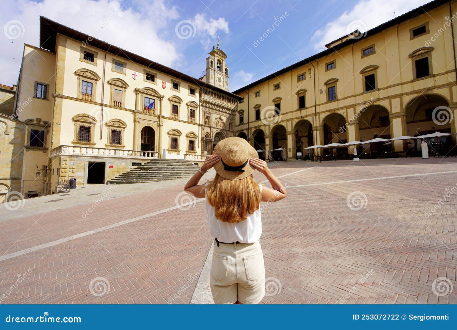 traveling in tuscany. back view of tourist girl holding hat in piazza grande square in the historic town of arezzo, tuscany, italy