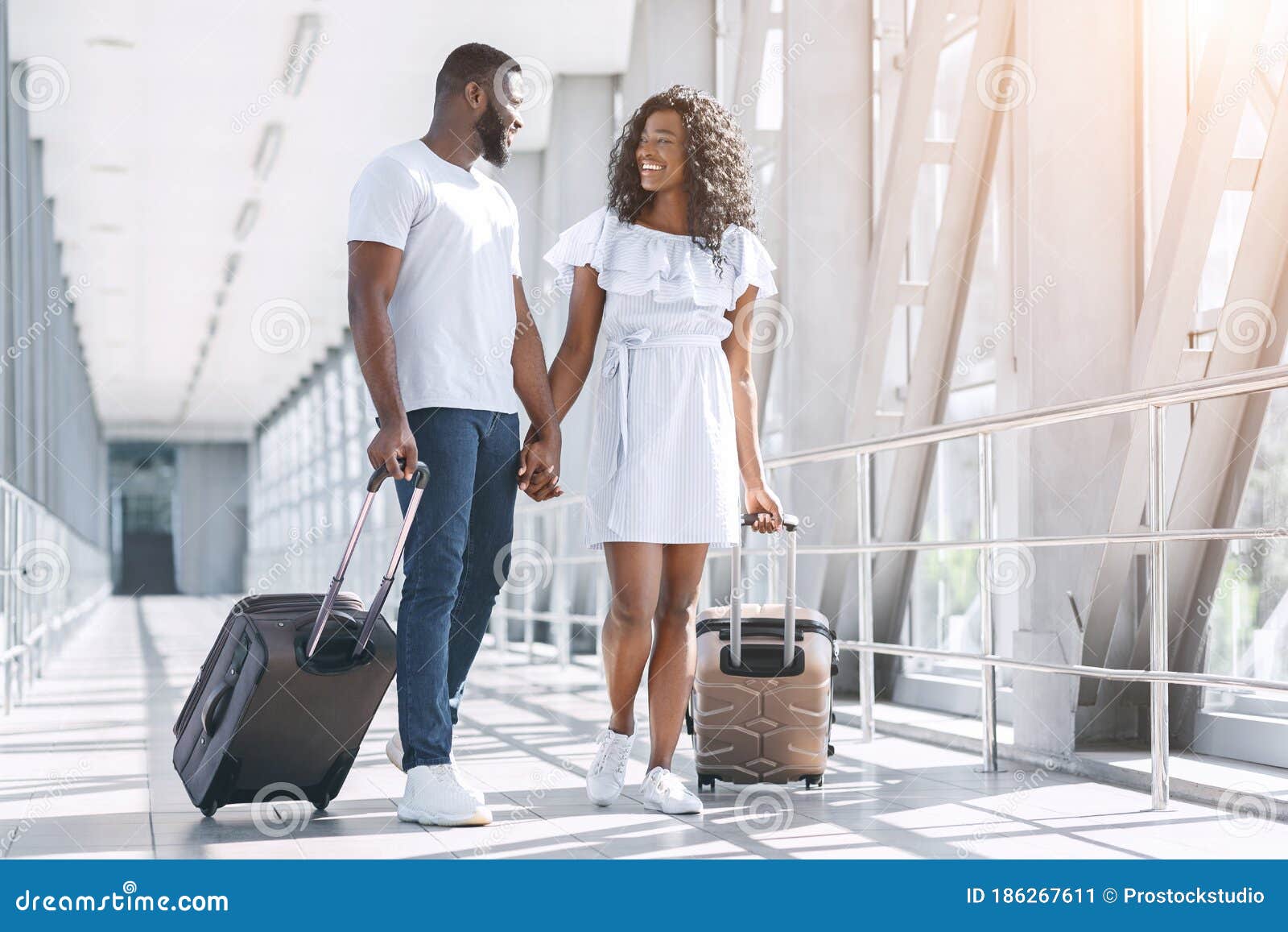 affectionate black couple enjoying honeymoon trip, walking with suitcases in aiport