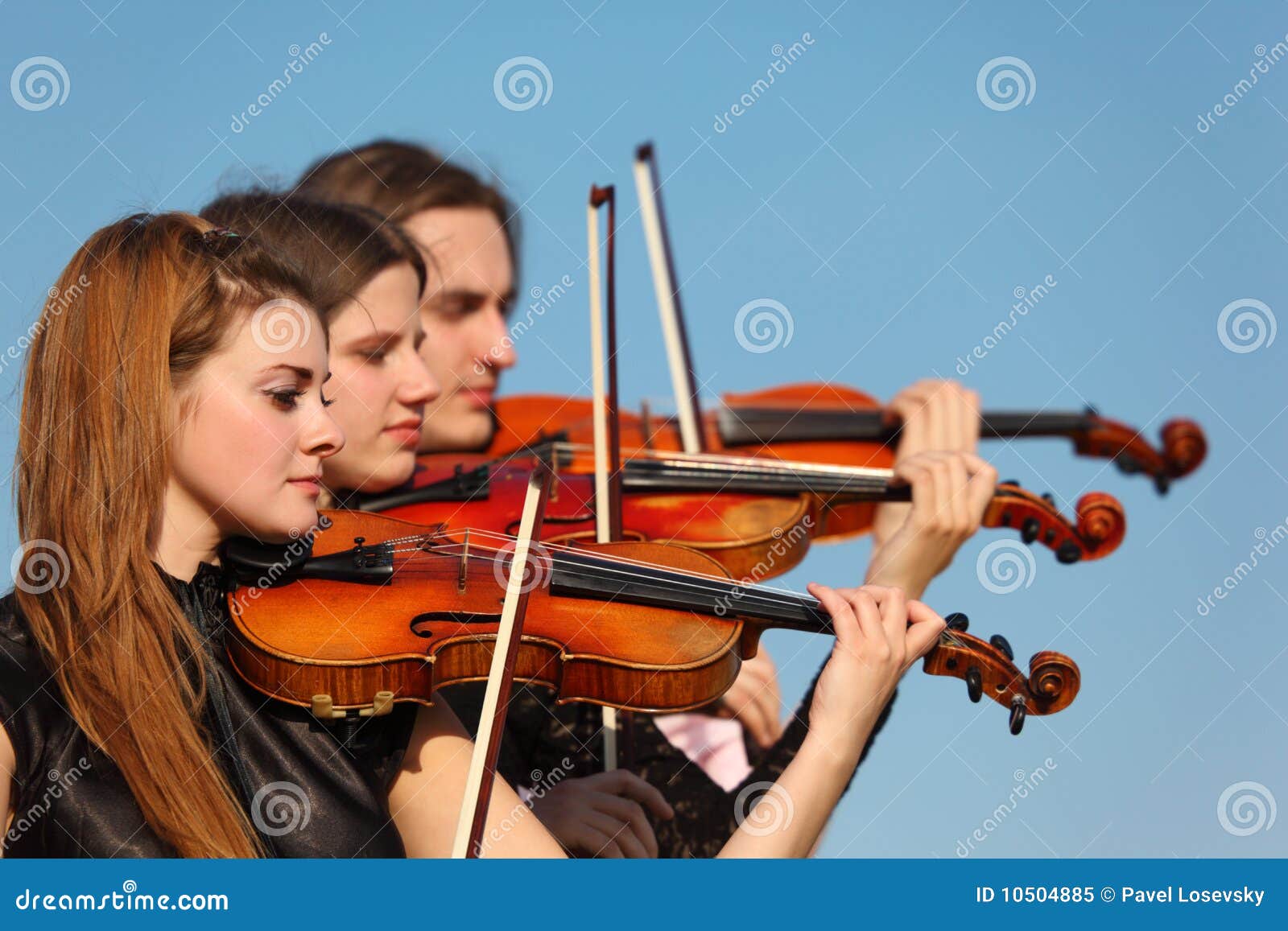 trio of violinists plays against sky