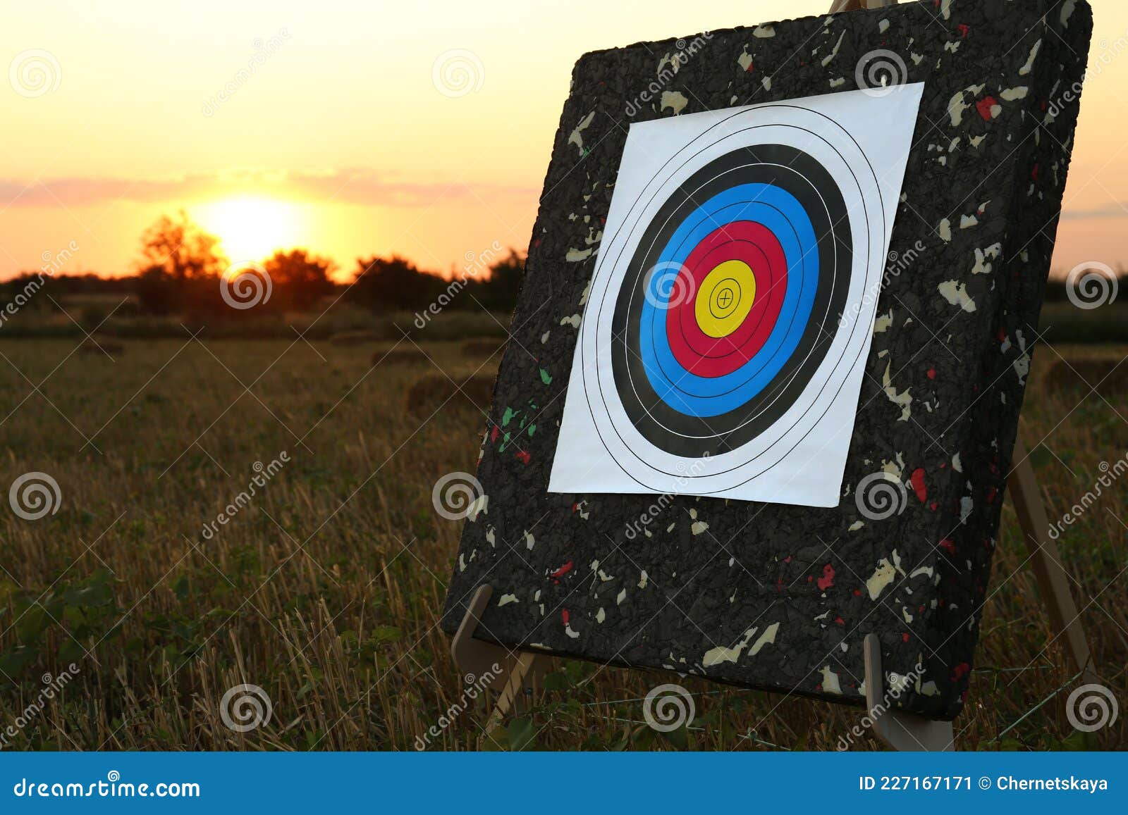 tripod with archery target in field at sunset
