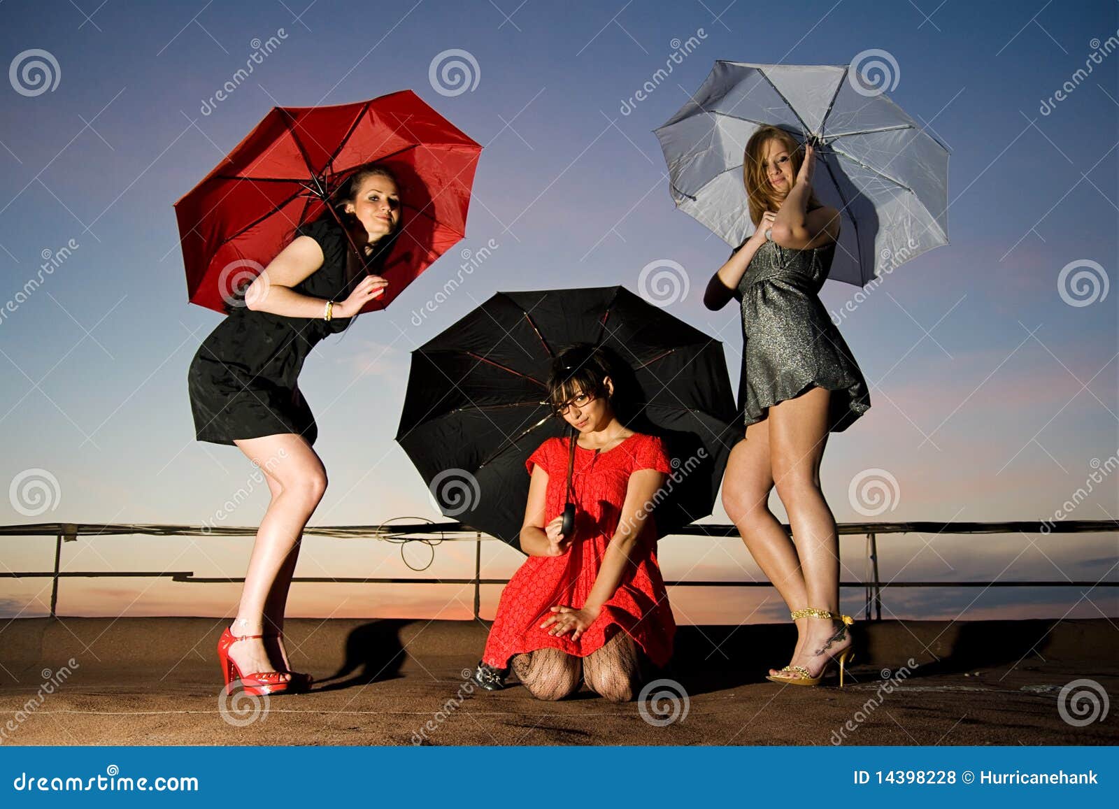 Trois nanas sexy avec la pose de parapluies. Jeunes femmes attirants dans des robes courtes sur le toit