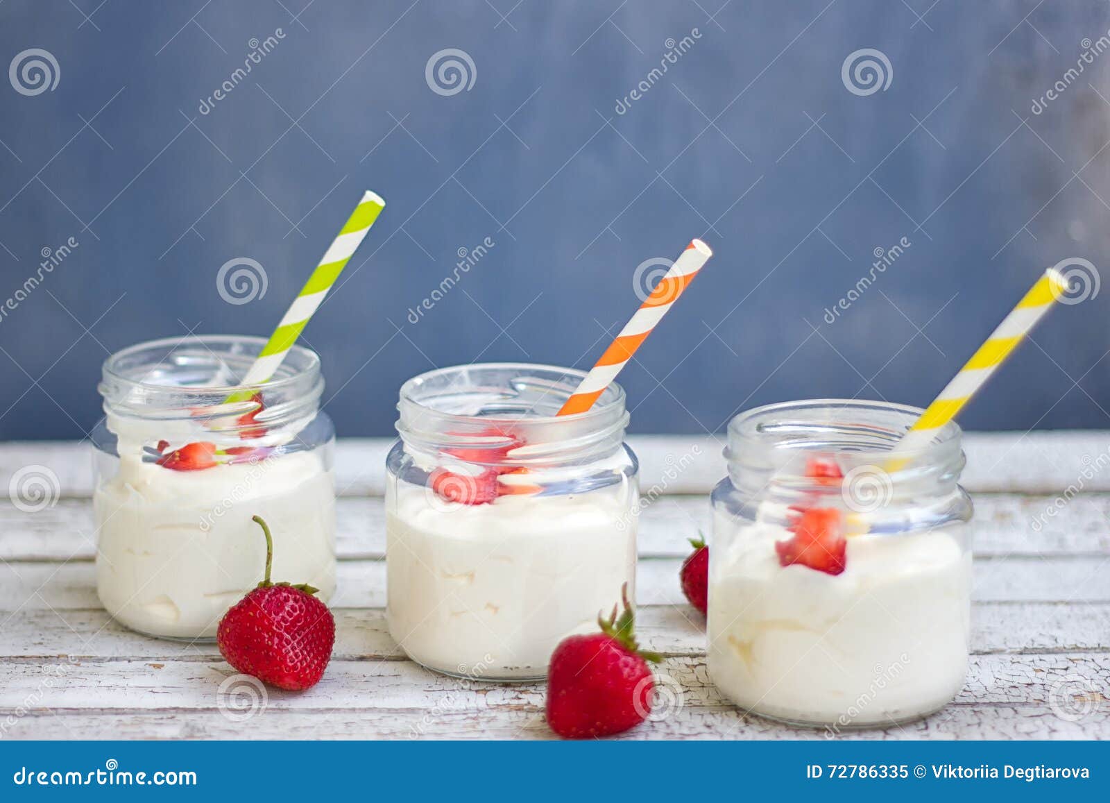 Trois pots de yaourt avec des fraises et des tubes colorés sur un conseil en bois