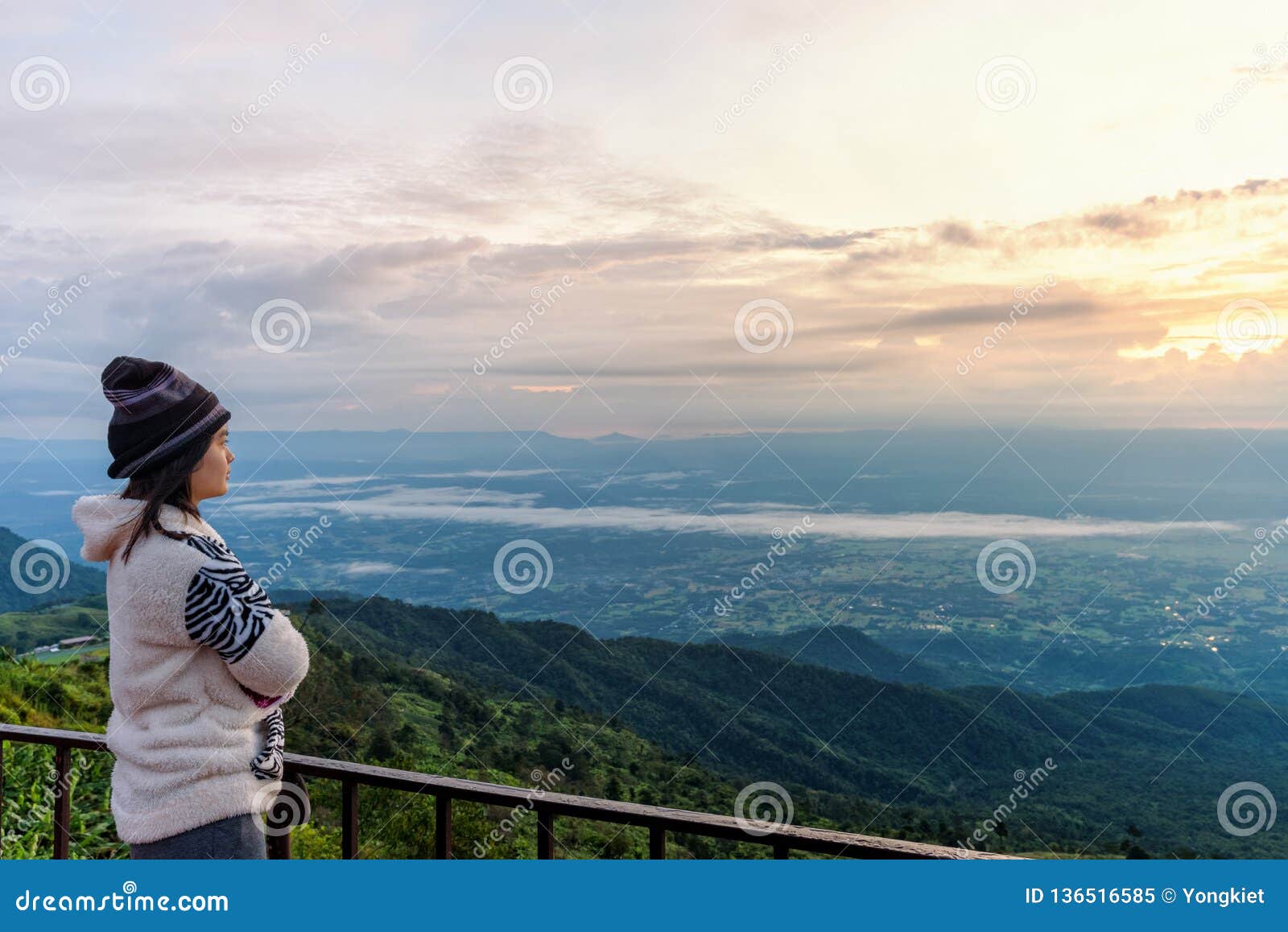 Turista de la mujer que mira la salida del sol. Turista de la mujer en una situación del vestido del suéter que mira el paisaje hermoso de la naturaleza del bosque y de la montaña durante la salida del sol en el alto pico por la mañana en el punto de vista Phetchabun, Tailandia de Phu Thap Boek