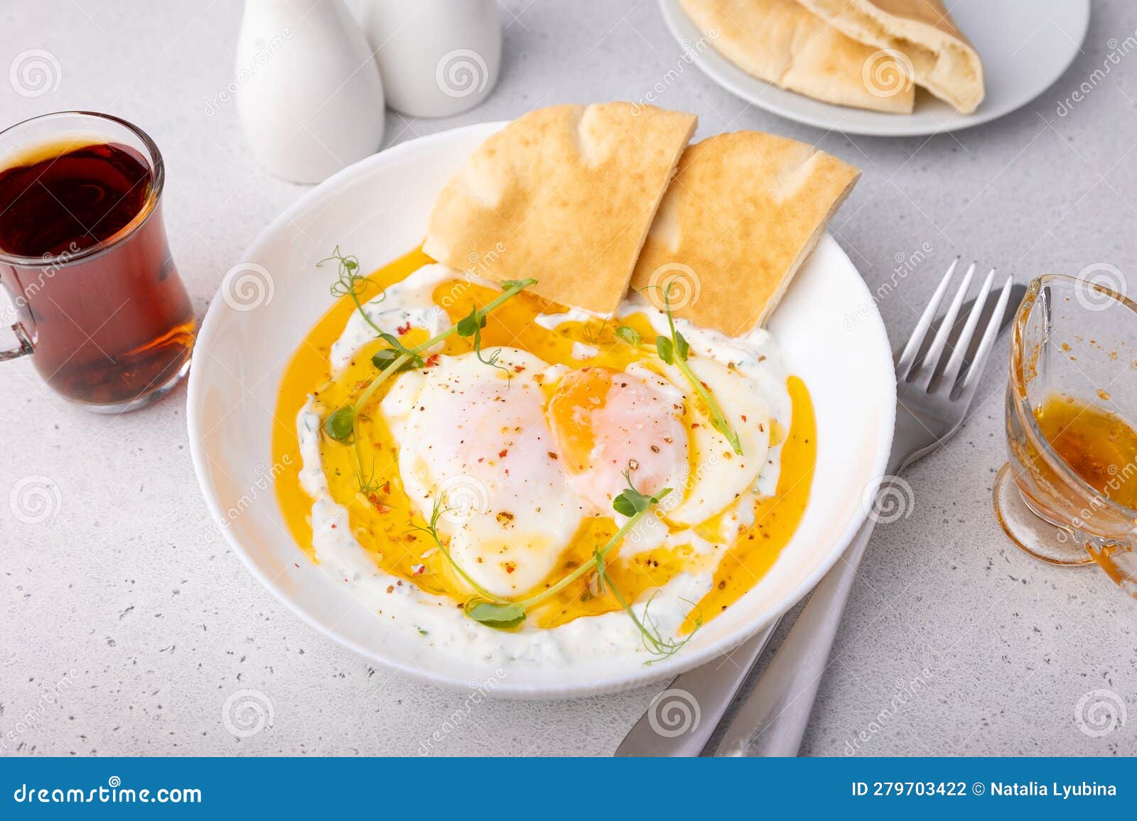 turkish eggs (chilbir) with yogurt, fragrant butter, pea sprouts, flatbread and tea. traditional turkish breakfast.
