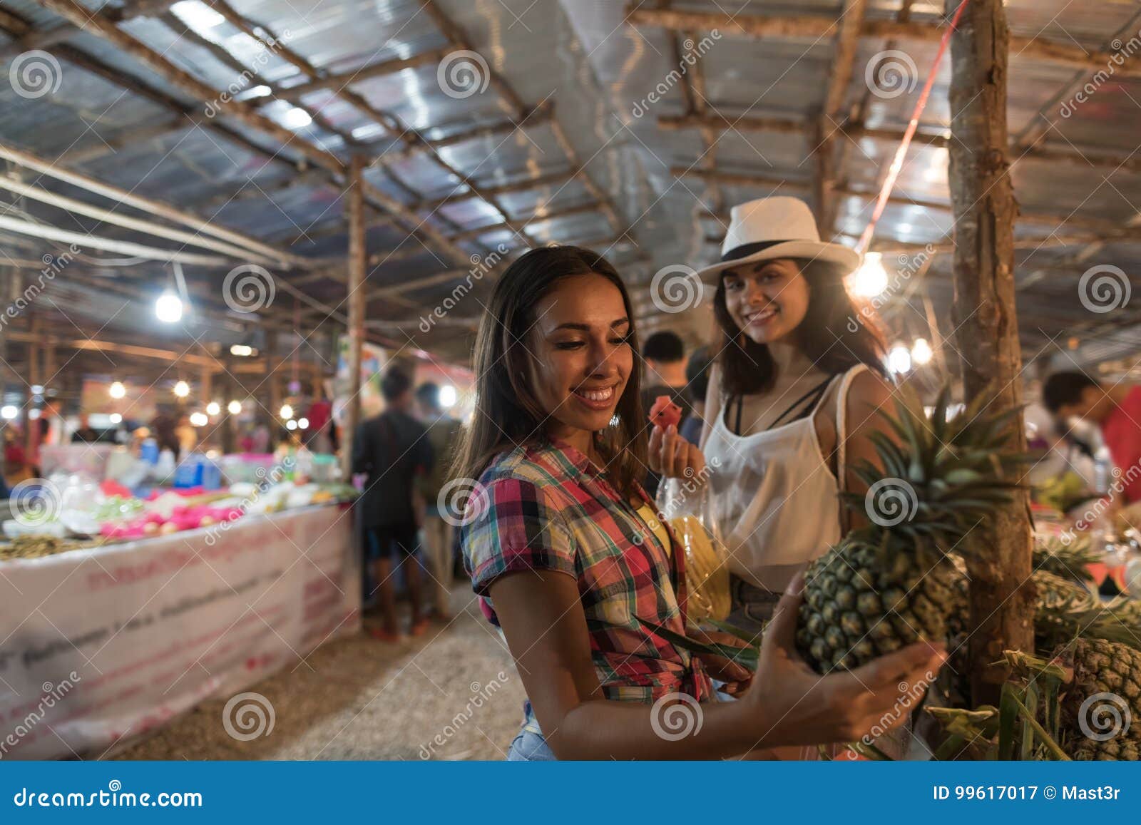 Två kvinnliga turister väljer ananas på tropiska unga kvinnor för gatamarknaden som köper nya frukter på asiatisk basar