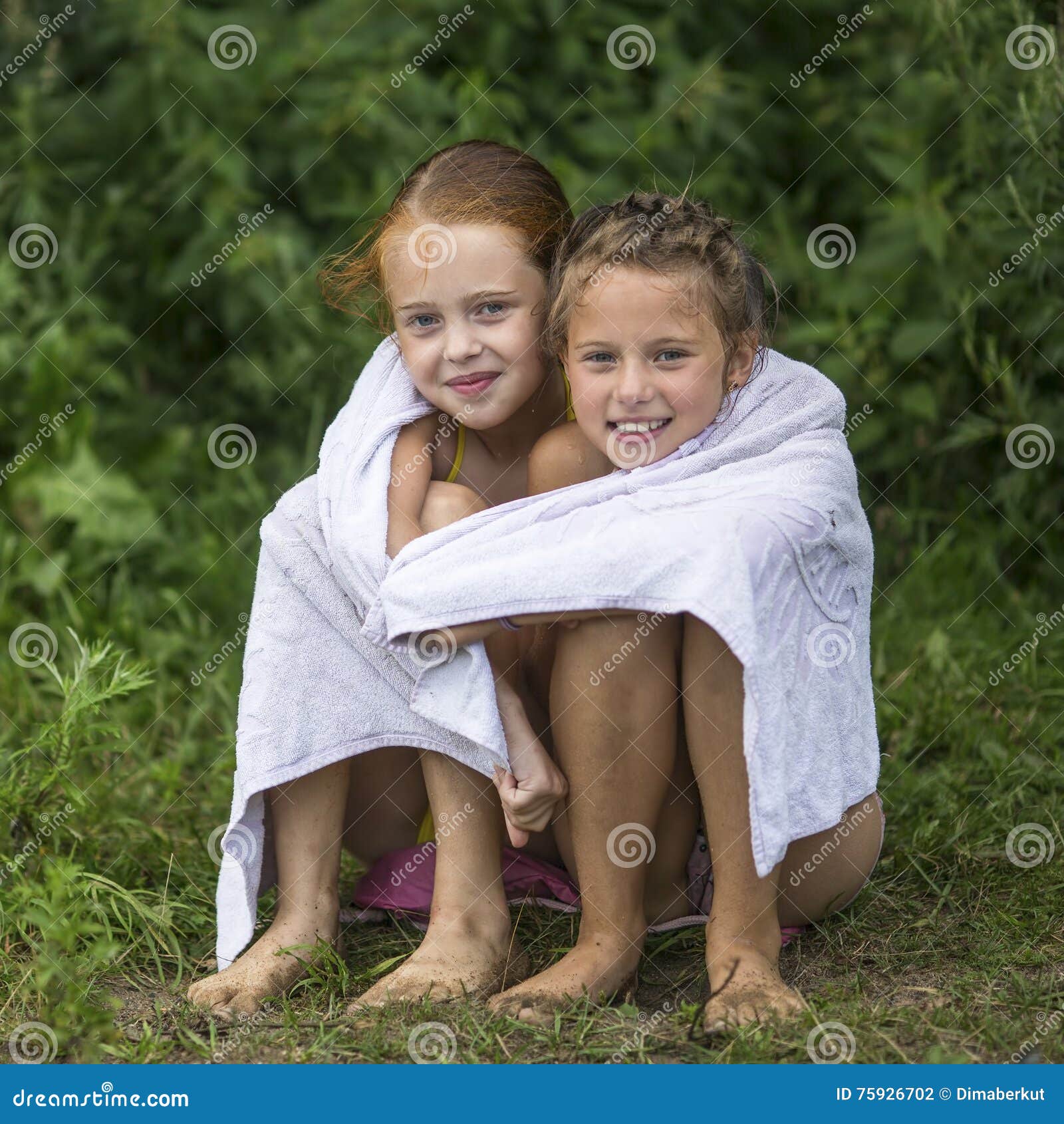 Två Stygga Små Flickor Som Sitter På Stranden I En Handduk Efter Ett Bad I Sjön Sommar Arkivfoto