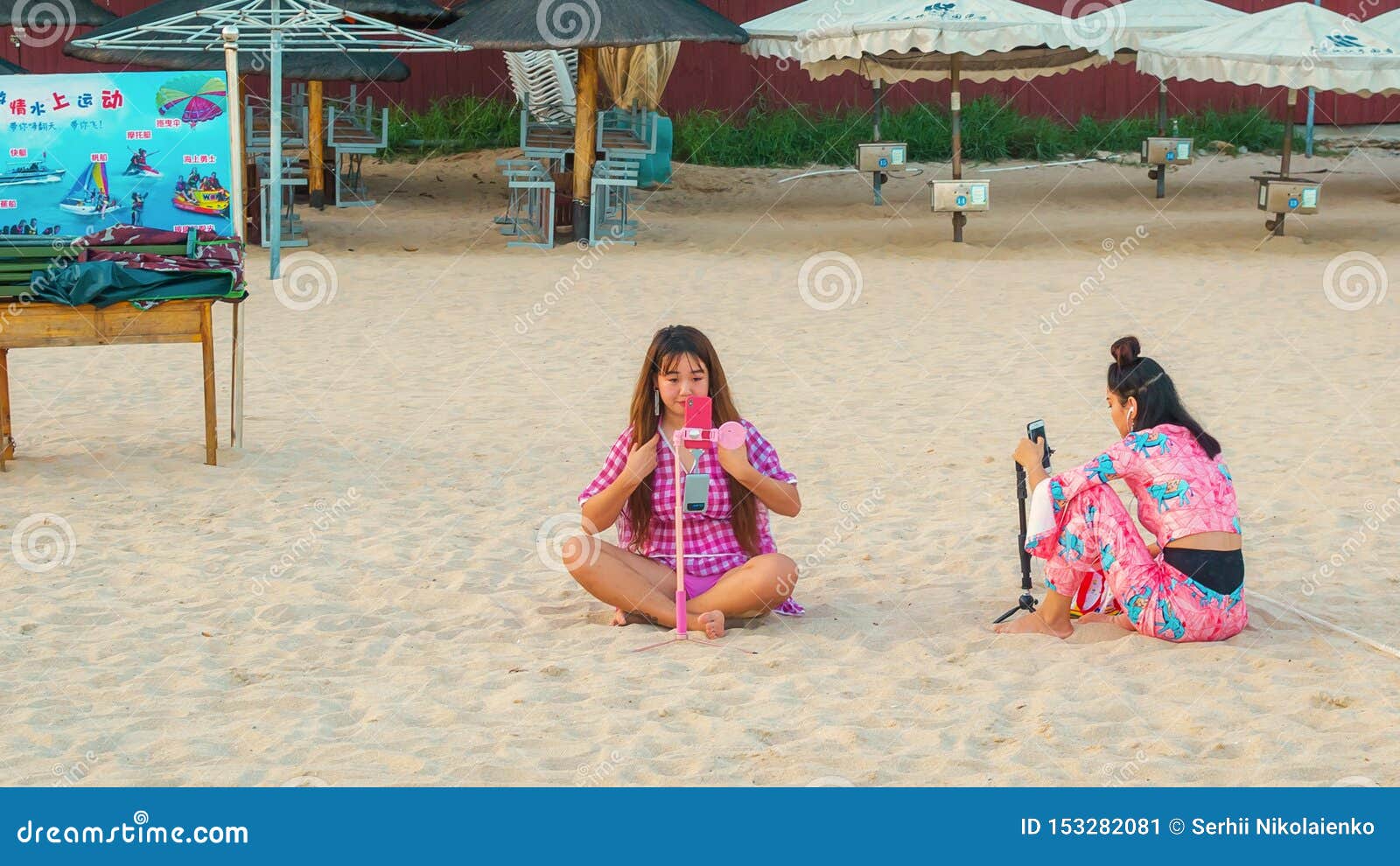 Sanya, Hainan, China - Mei 17, 2019: Twee jonge Chinese meisjes op het strand, die op het zand zitten, nemen een selfie Online is de rapportering een populaire activiteit onder de Chinese jeugd
