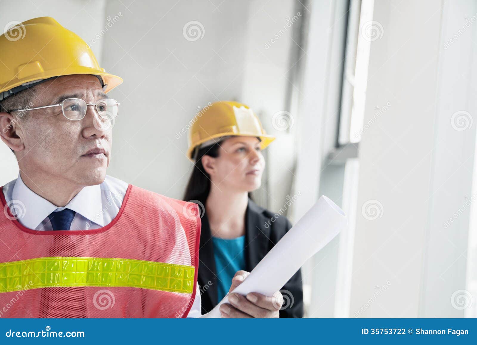 two architects in protective workwear and hardhats working in an office building