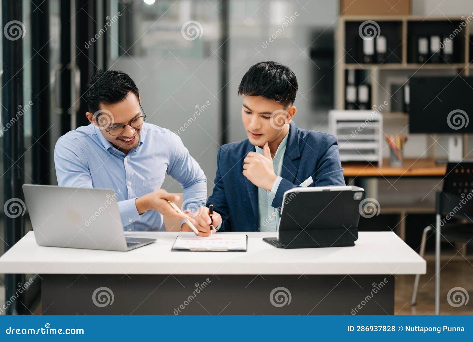 two asian business workers talking on the smartphone, tablet and using laptop at the office