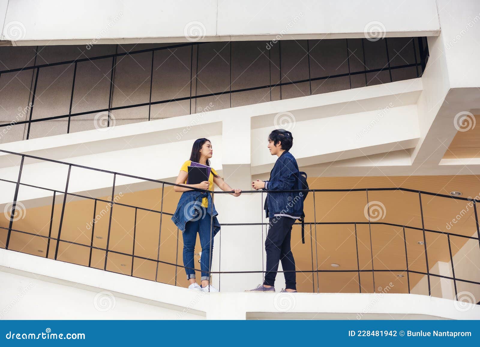 two asian university students walking and conversing to class in a magnificent campus building`s walkway