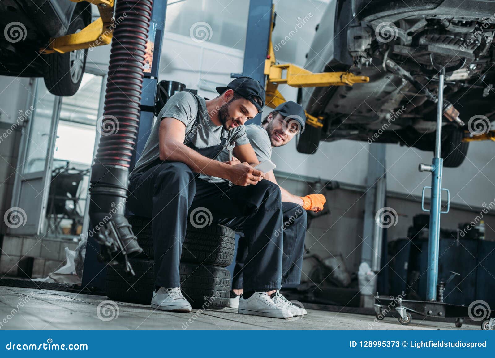 two auto mechanics using smartphone and resting in auto