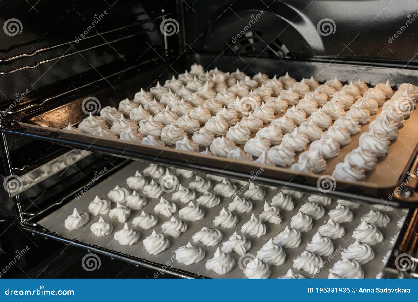 Two Baking Sheets with White Small Meringues Stand in Rows and Cook in