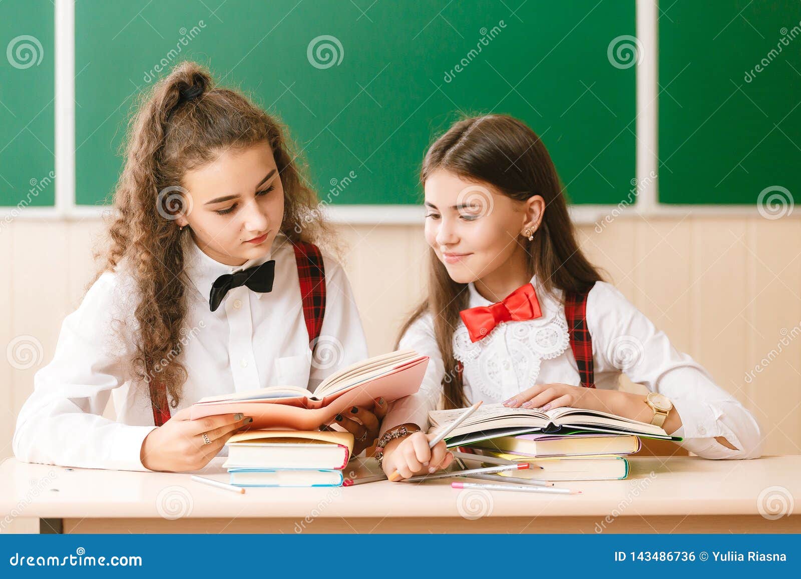 Two Beautiful Schoolgirls Are Sitting At The Desk With Books In The