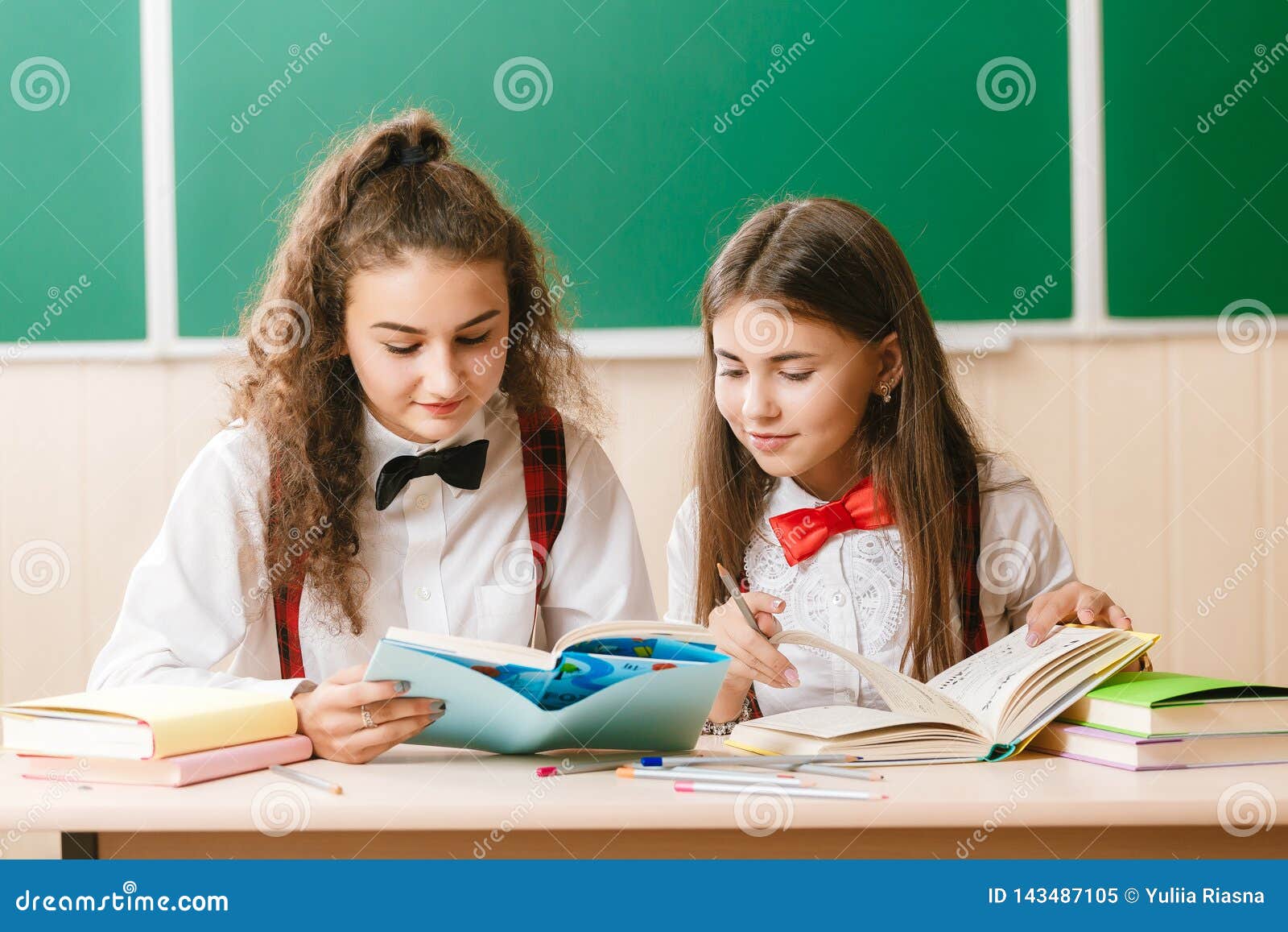 Two Beautiful Schoolgirls Are Sitting At The Desk With Books In The 