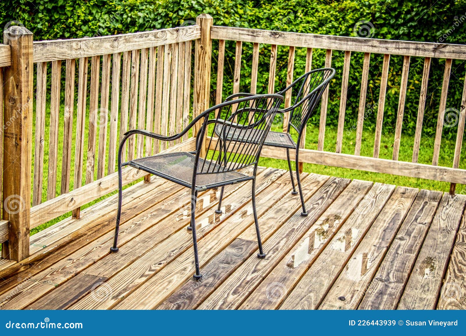 Two Black Metal Lawn Chairs Sitting by Rail on Wooden Deck after