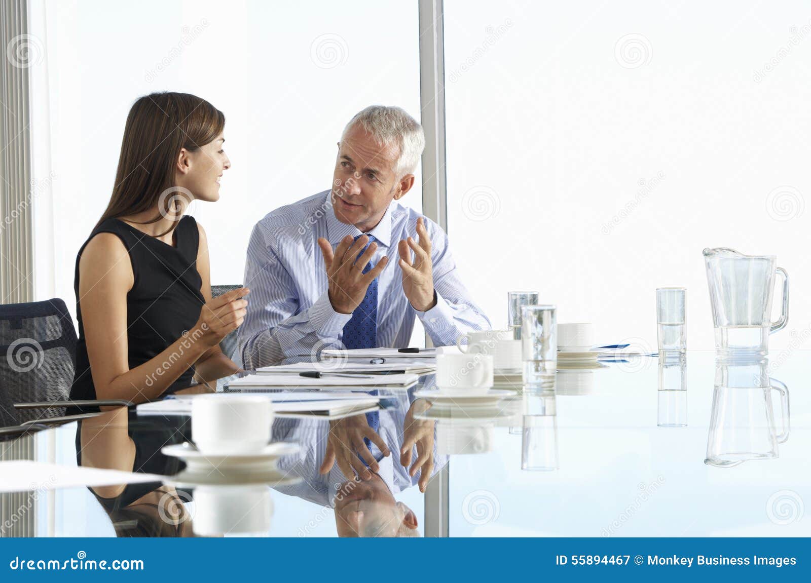 two business colleagues sitting around boardroom table having informal discussion