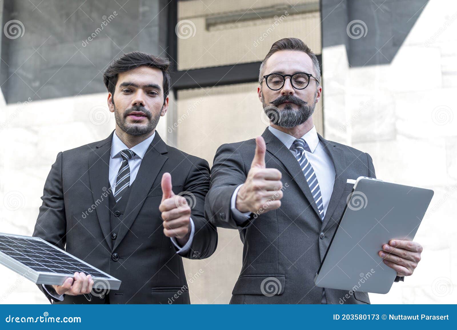 two businessmans trumps up and holding power solar cell and laptops computer with smile confident on site new project power