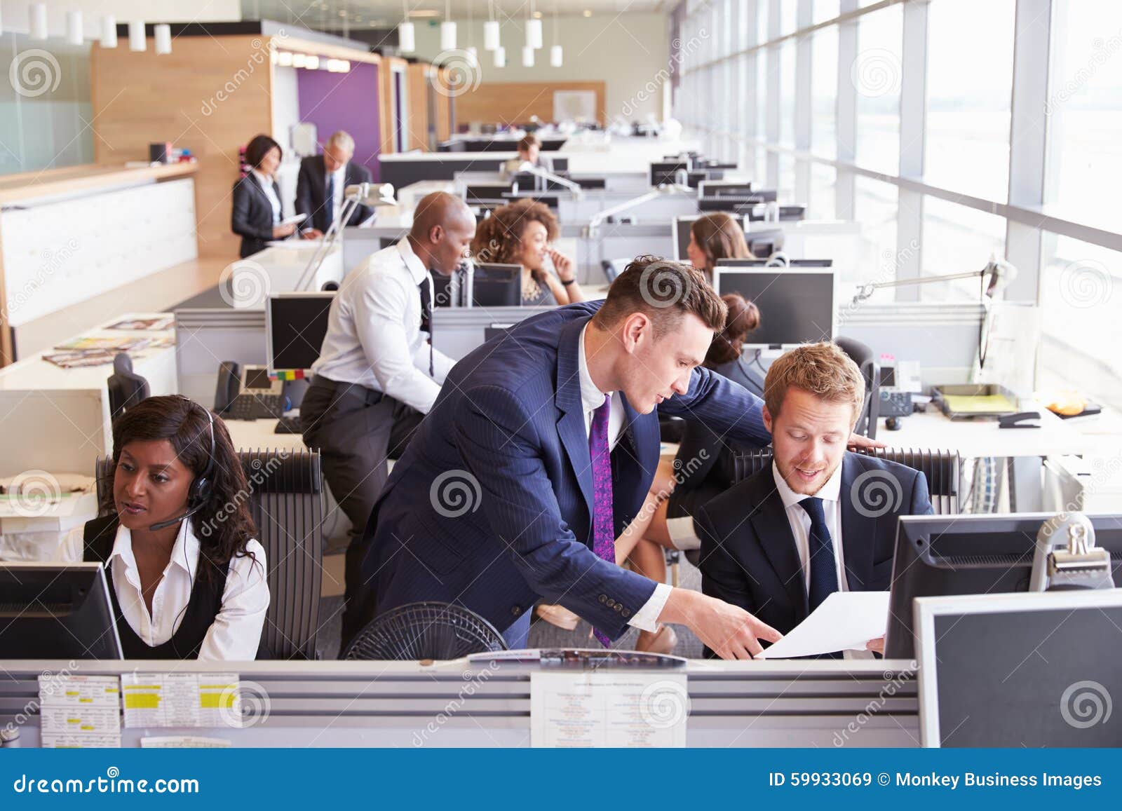 two businessmen discussing work in a busy, open plan office