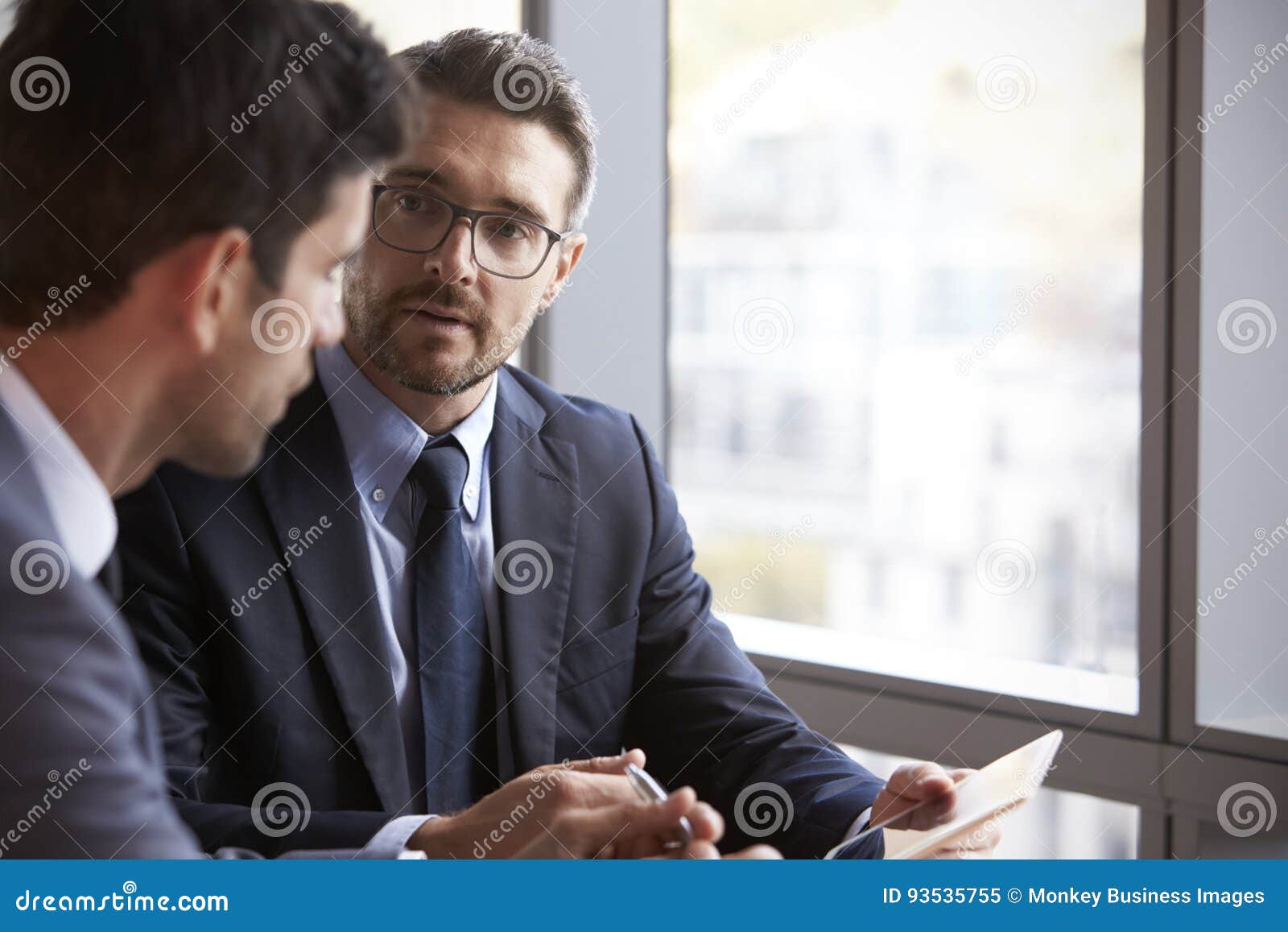 two businessmen using digital tablet in office meeting
