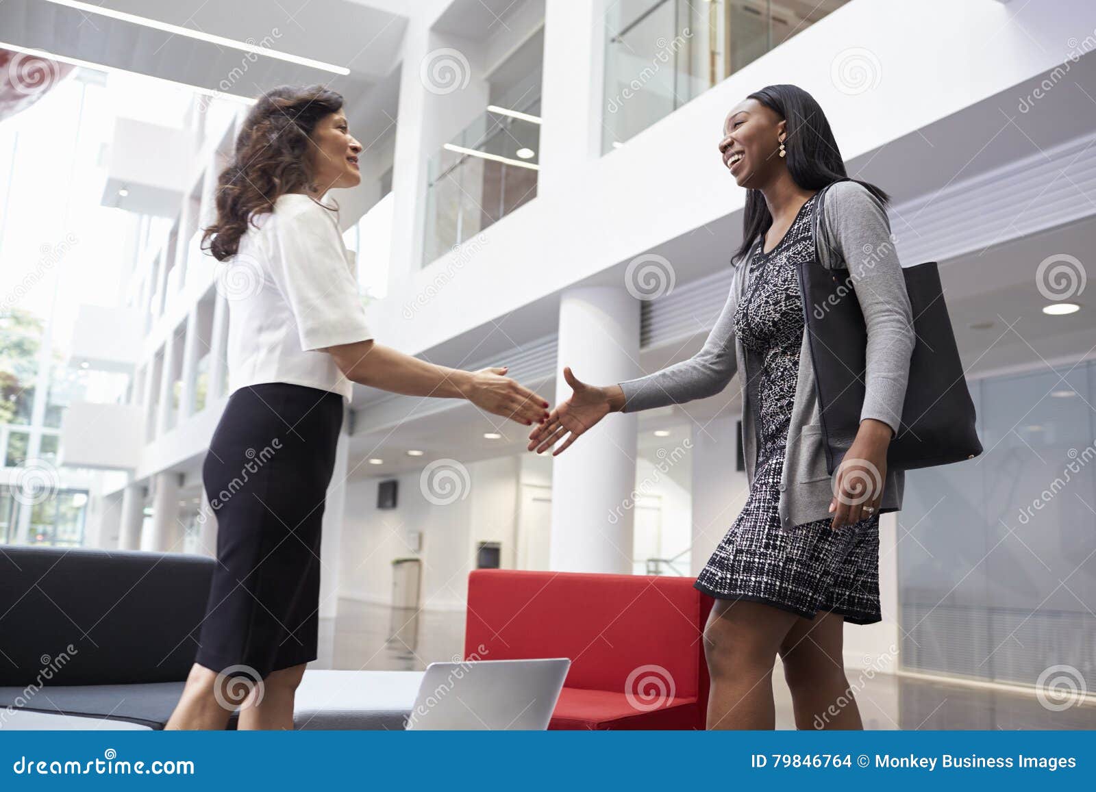 two businesswomen shaking hands in lobby of modern office