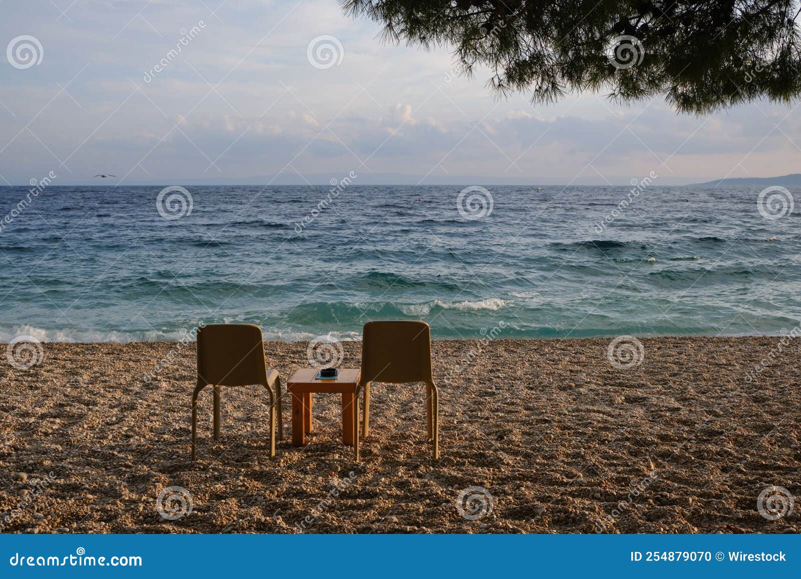 Two Chairs and Small Table on the Sandy Beach Facing the Sea Stock