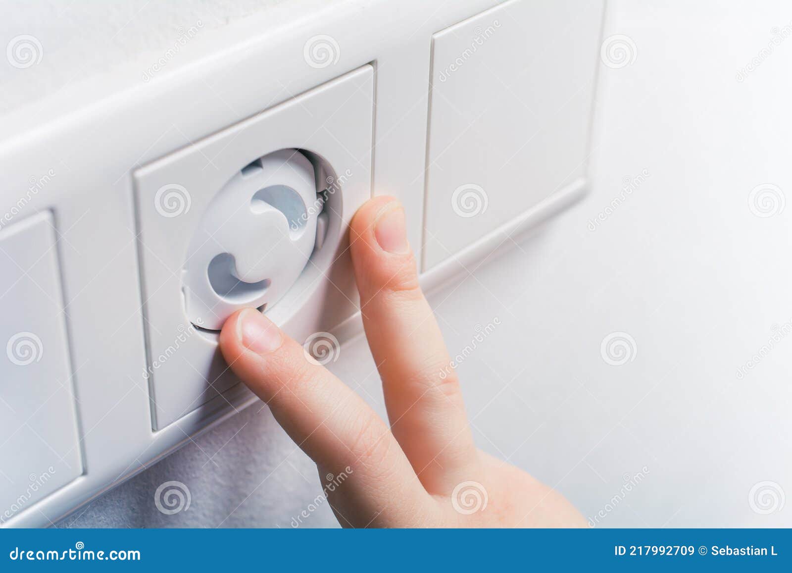 Two Child Fingers Touching a Wall Socket with Safety Plugs Prevent