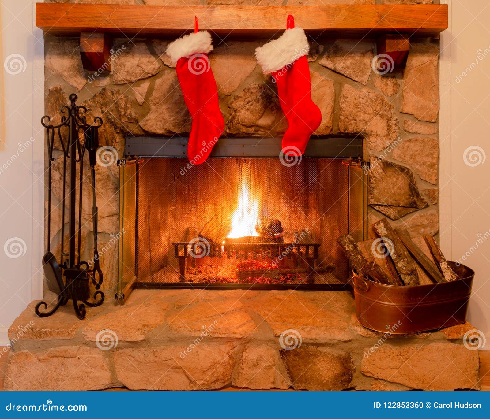 two christmas stockings on the mantle of a stone fireplace with a warm fire.