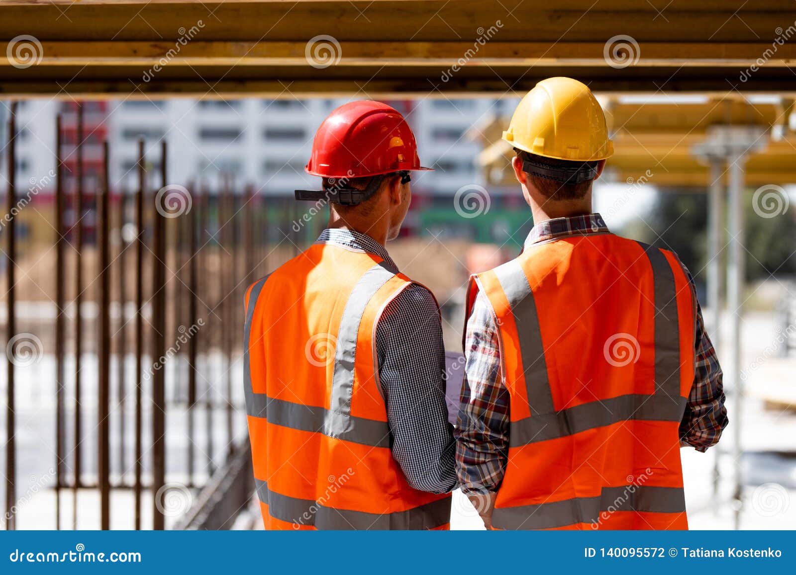 Two Civil Engineers Dressed In Orange Work Vests And Helmets Discuss
