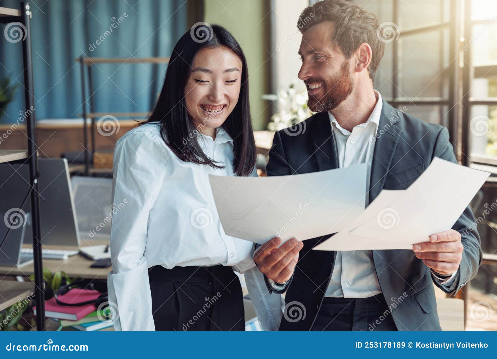 Two Colleagues Looking on Documents and Smile Standing in Office Stock