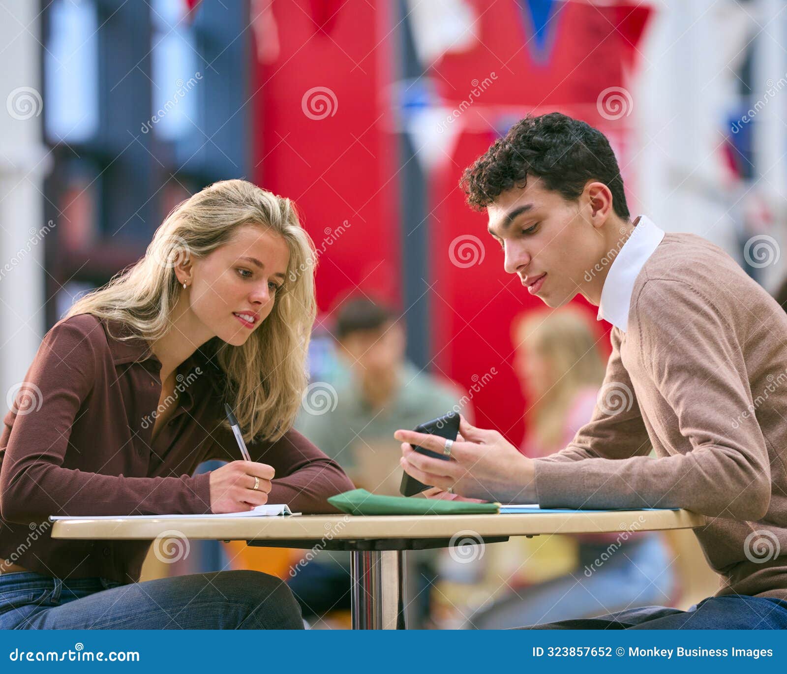 two college or university students with mobile phone working together in study area