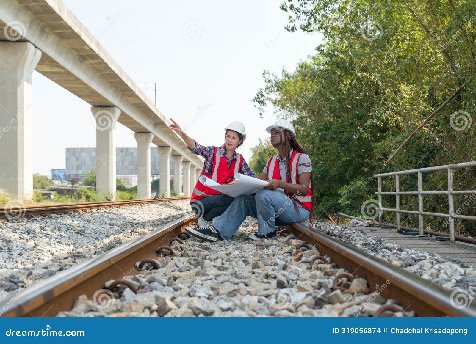 two construction or engineer with safety helmet and high-visibility vest reviewing work to be done or progress on a railway track