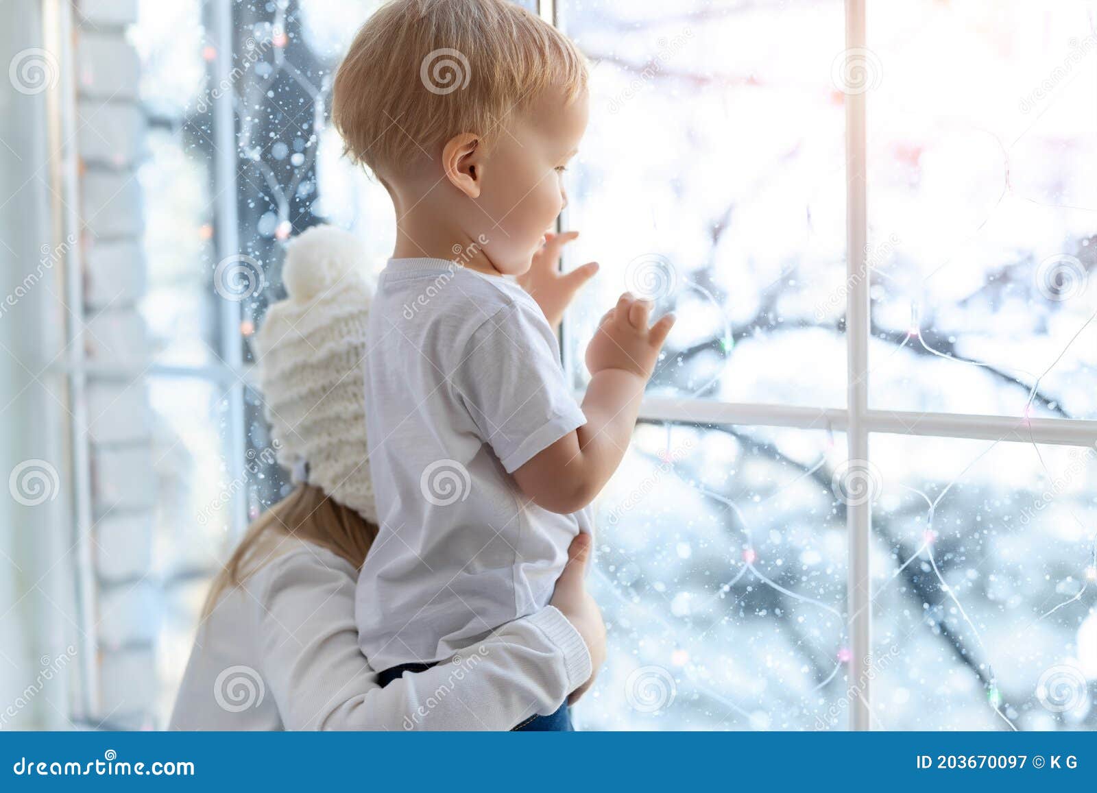 two cute adorable little blond cauasian children siblings stay near window and looking outside waiting for snow, wonders