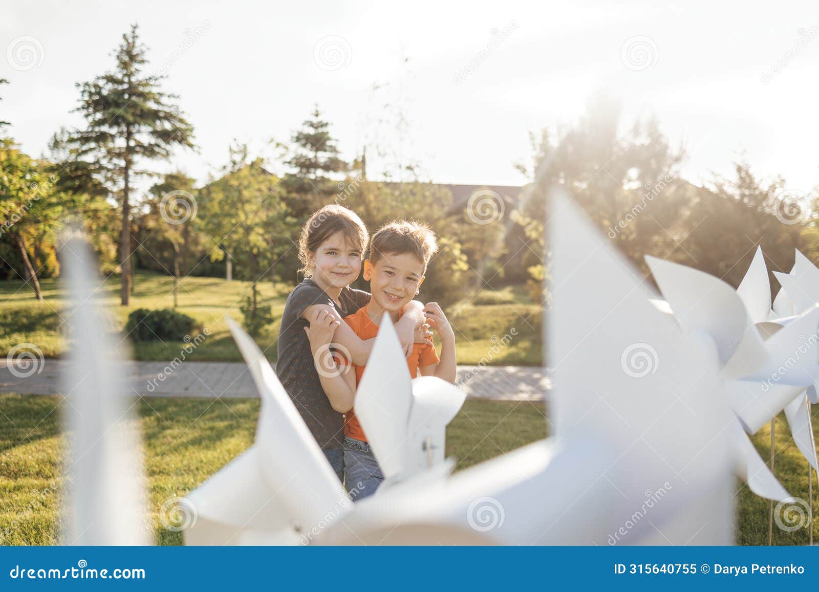 two cute kids cuddle in the backyard of the house. brother and sister near the white wind turbines. a boy and a girl have fun on a
